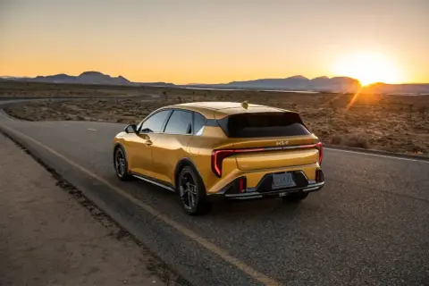 Un coche hatchback amarillo brillante recorre una carretera desierta al atardecer, con las montañas al fondo.