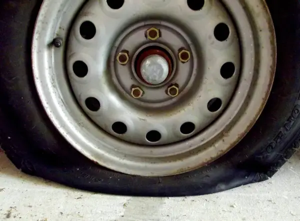Un clavo en rueda coche ha causado un pinchazo. La llanta metálica y el neumático desinflado se ven sobre el suelo de cemento.